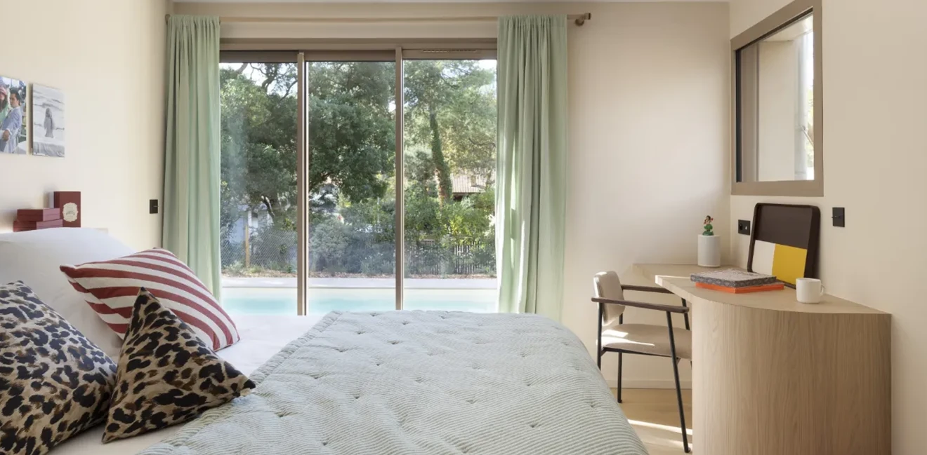 Vue sur la piscine et la forêt landaise depuis les grandes baies vitrées d'une chambre